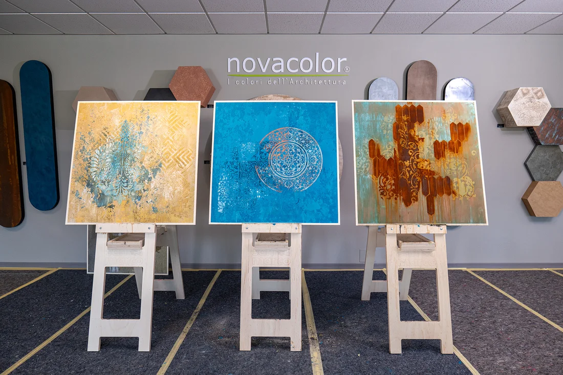 Tre pannelli decorativi realizzati durante il corso, su cavalletti davanti alla parete Novacolor